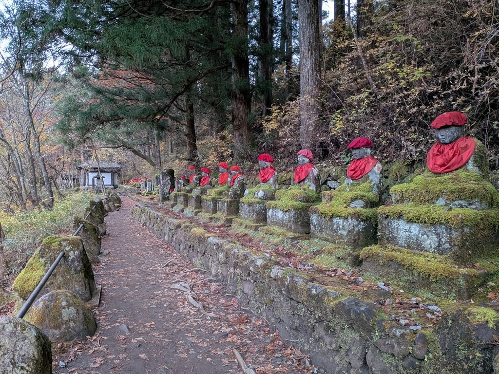 A serene row of Jizo statues with red bibs lined along a mossy path in Nikko, Japan during fall.
